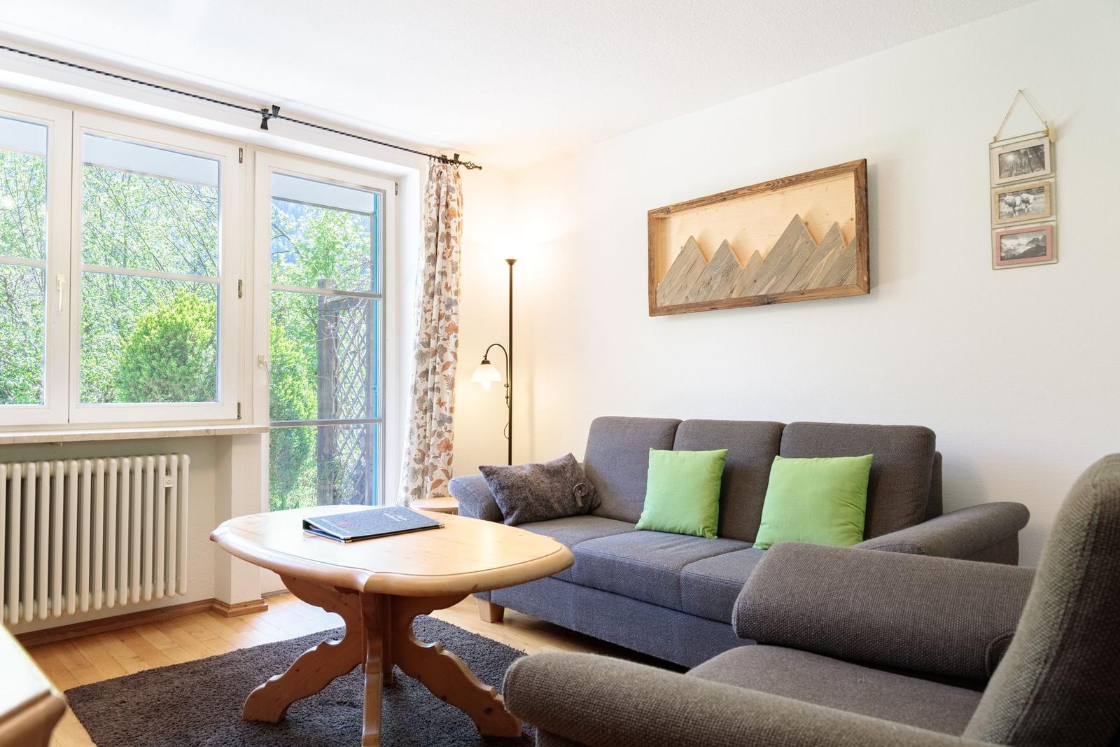 Living room with sofa, table, and view of greenery through window.