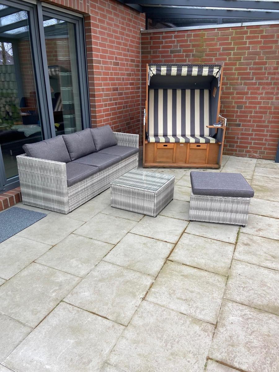 Terrasse mit Rattan-Sofa, Beistelltisch und Strandkorb. Fliesenboden und Backsteinmauer.