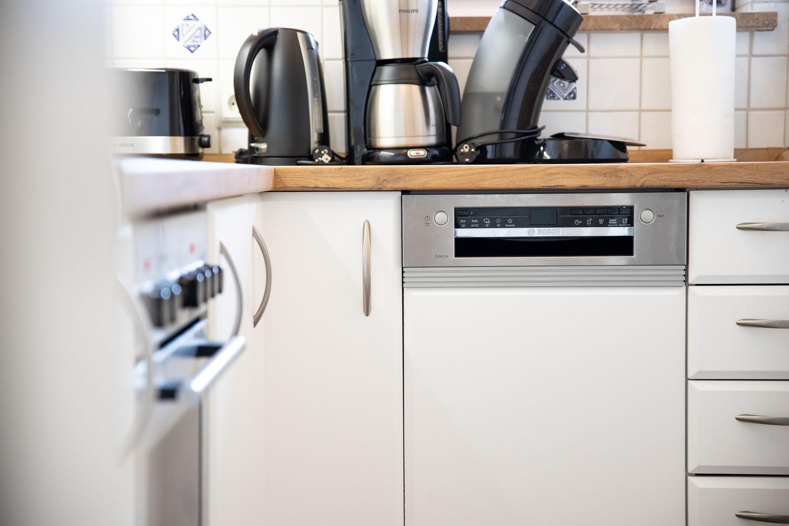 Kitchen with dishwasher, coffee machine, and kettle on wooden surface.