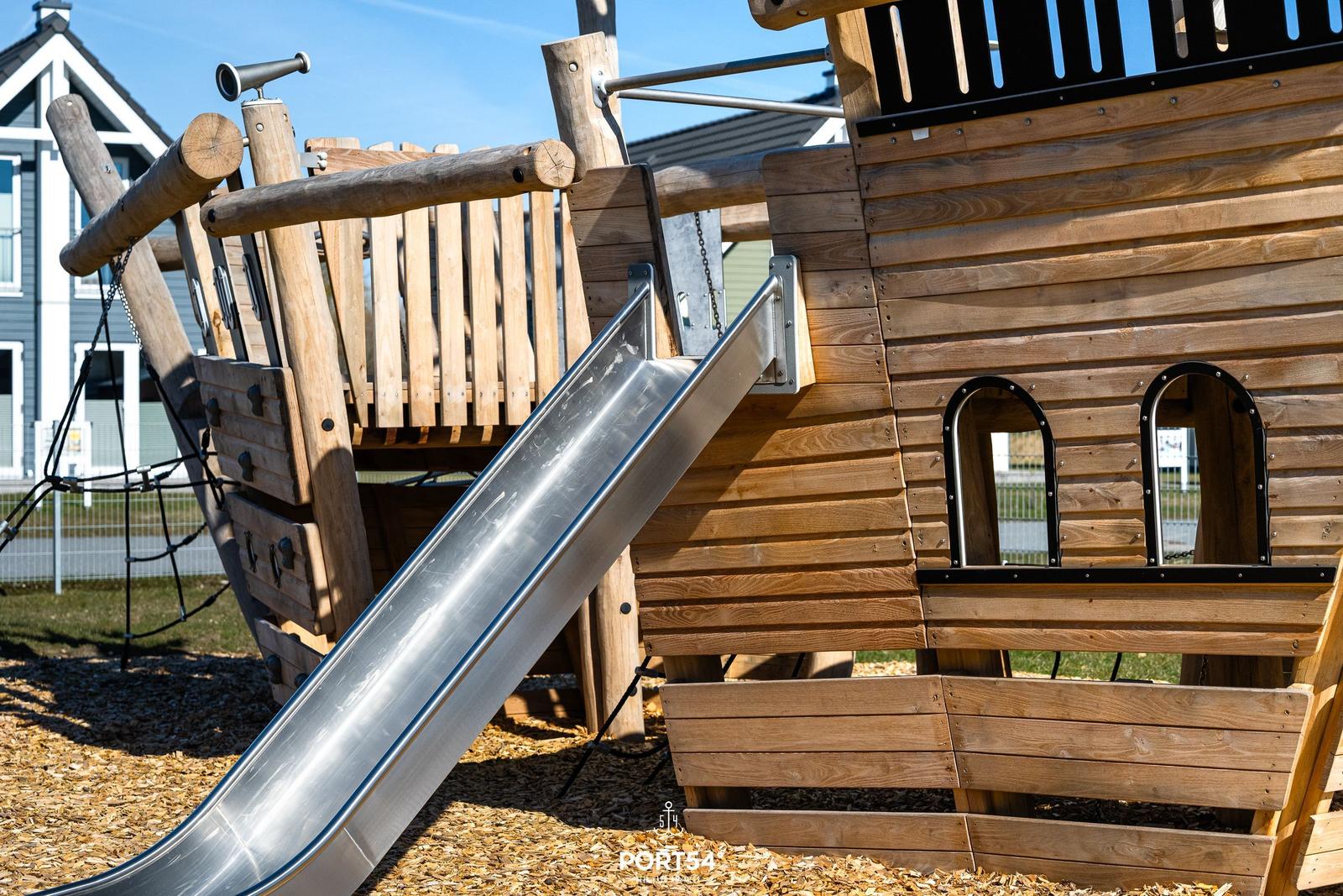 Holzspielplatz mit Metallschleife und Blickfenstern