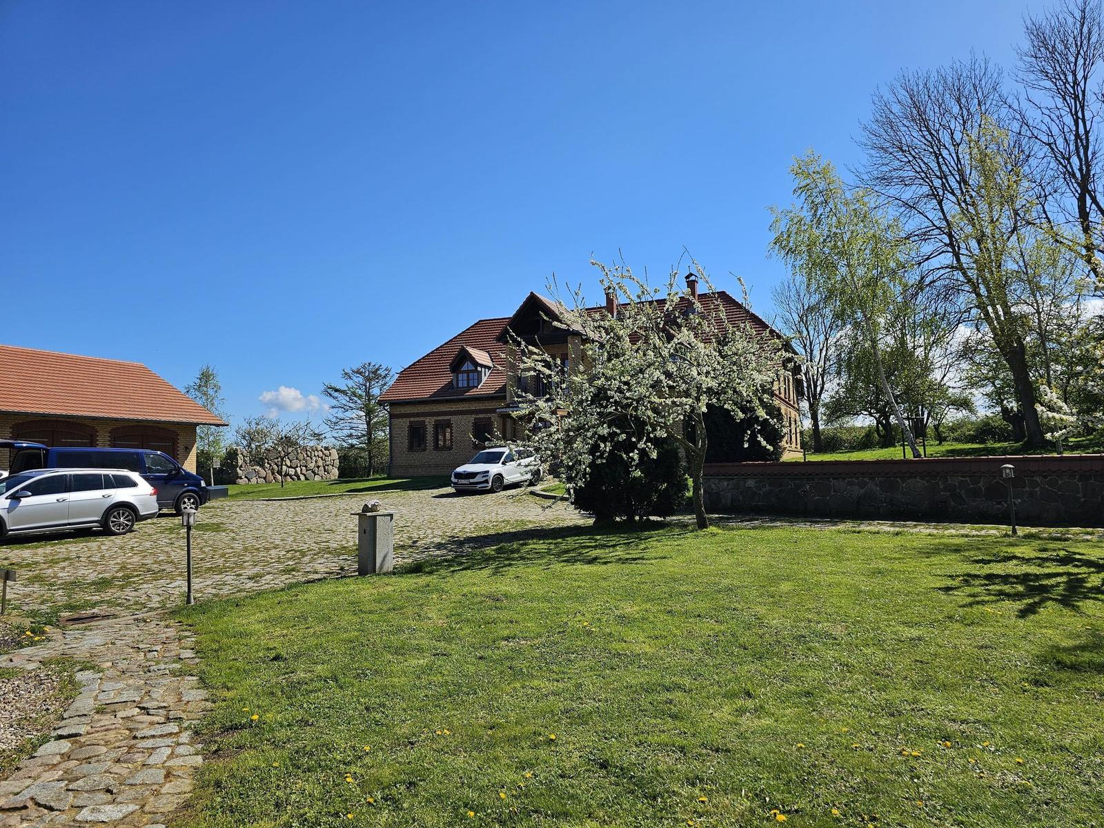 House with red roof, green lawn, and blue sky. Several cars parked in front of the building.