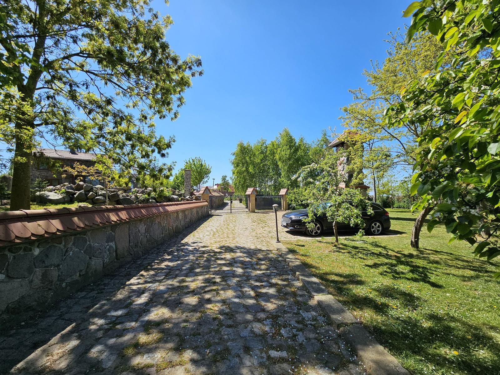 Stone wall and cobblestone path lead to entrance. Car parked on lawn.