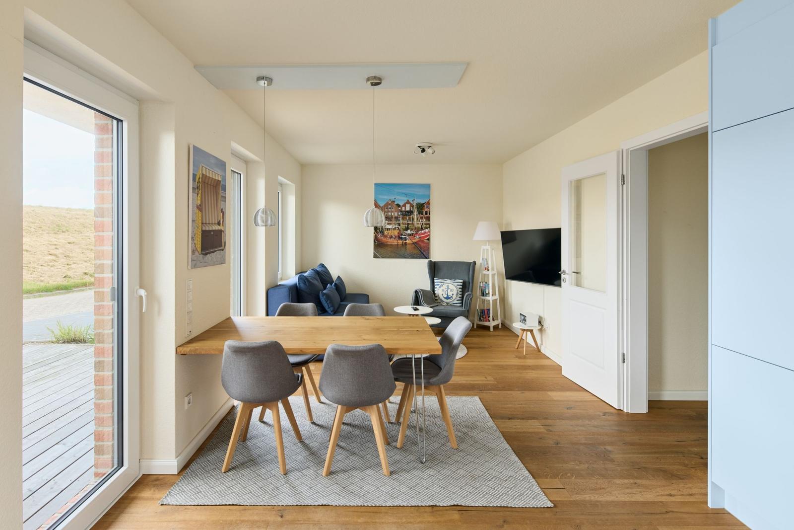 Essbereich mit Tisch und Stühlen, Wohnzimmer mit Sofa und Fernseher, Holzboden und große Fenster.