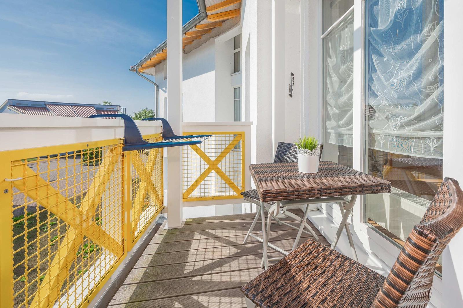 Terrasse mit Tisch, Stühlen und Pflanze. Gelb gestrichene Geländer.
