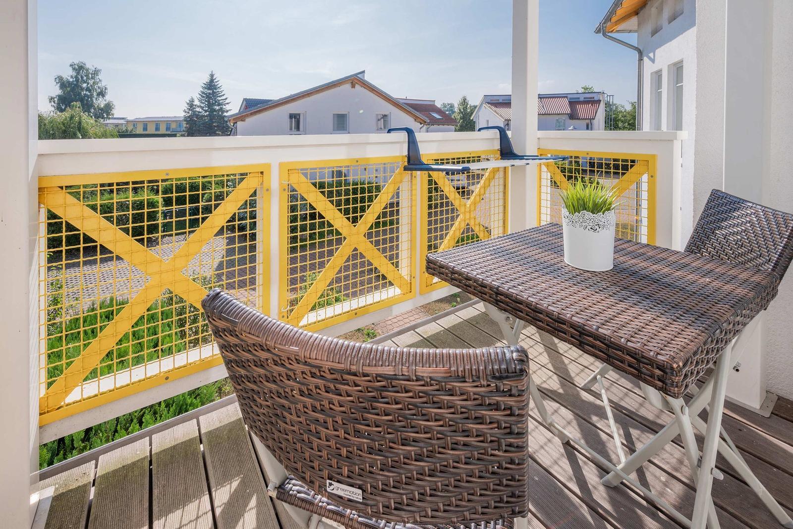 Terrasse mit Tisch und zwei Stühlen, gelbe Geländer und Blick auf Wohnhäuser.