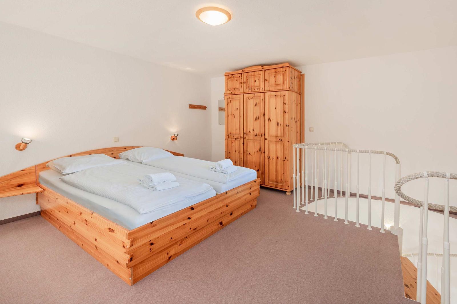 Schlafzimmer mit Holzbett, Kleiderschrank und Treppe