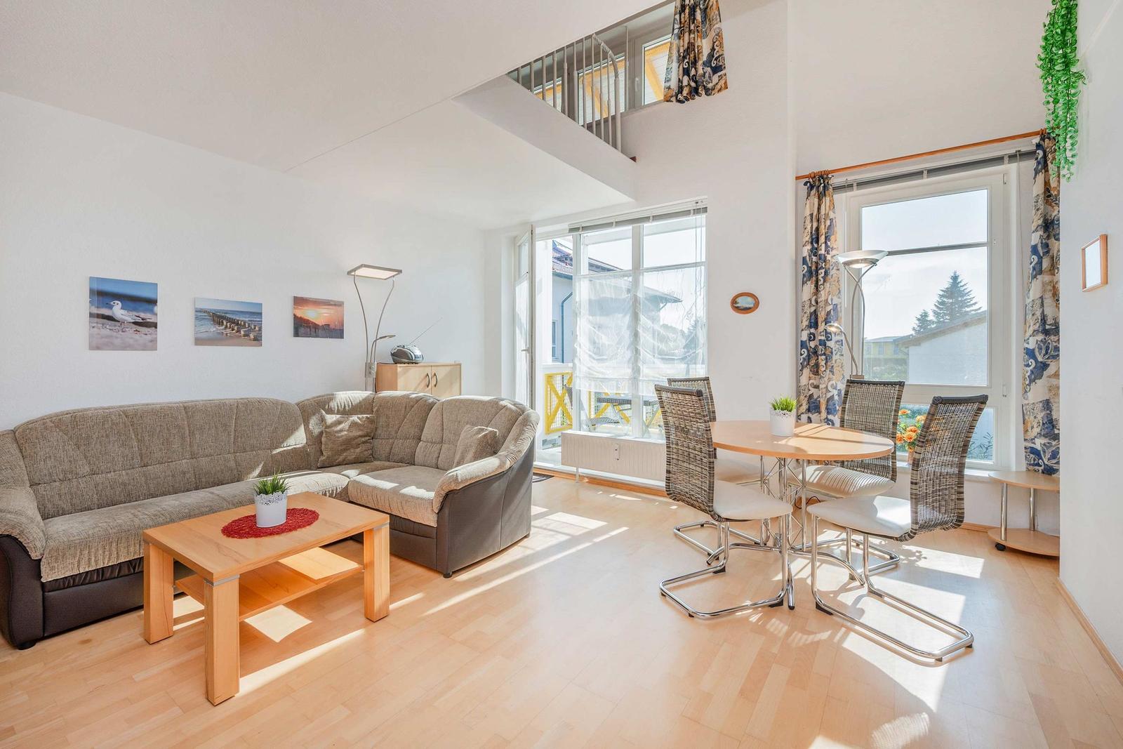 Wohn- und Essbereich mit Sofa, Tisch und Stühlen. Große Fenster und Lichtdurchflutung.