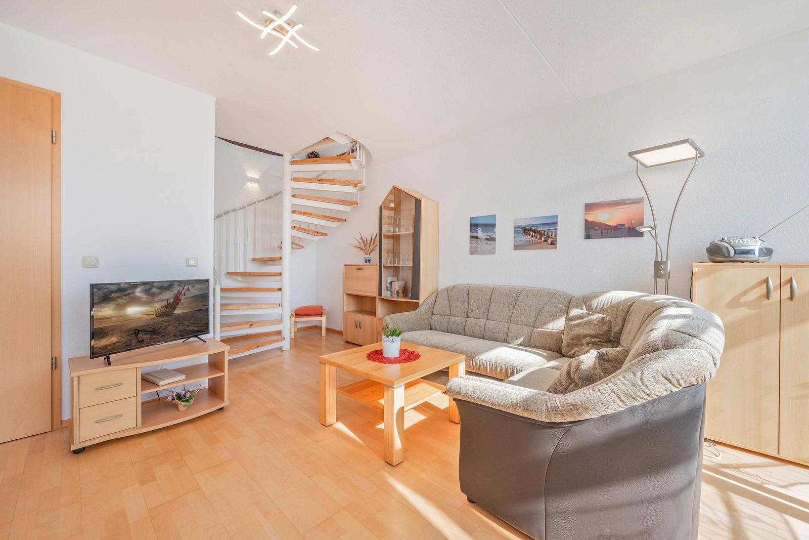 Wohnzimmer mit Sofa, Couchtisch, Fernseher und Wendeltreppe.