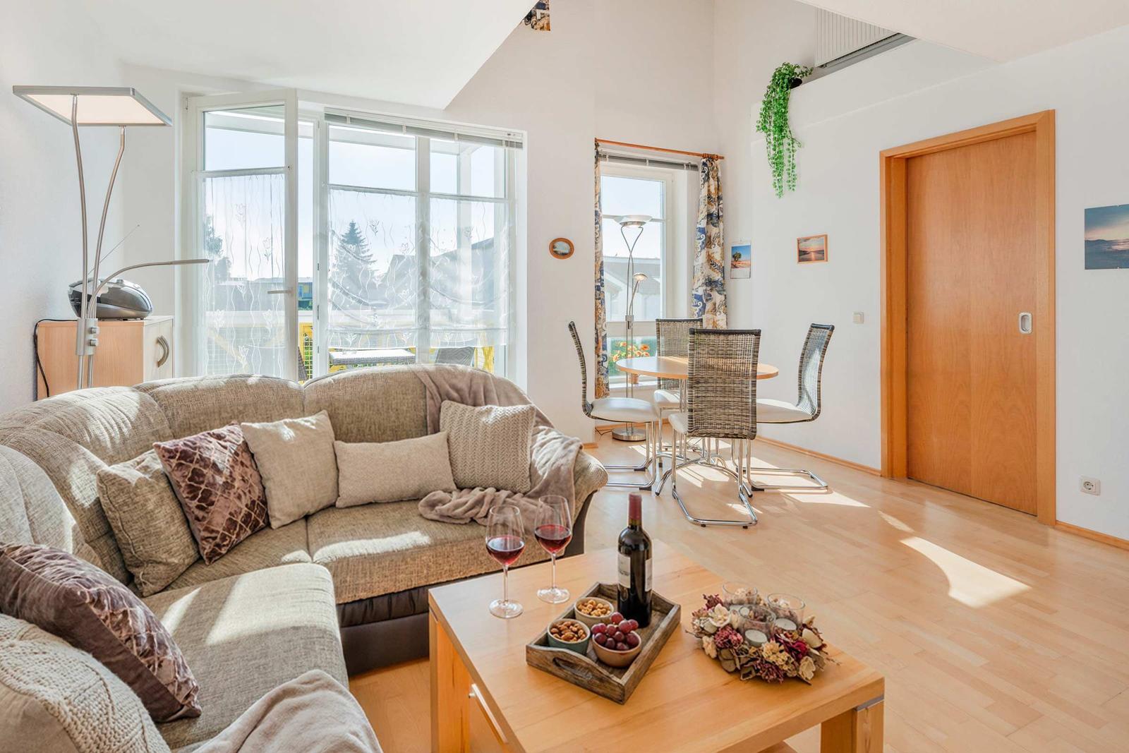 Wohn- und Essbereich mit Sofa, Tisch und Stühlen, großen Fenstern und Holzboden.
