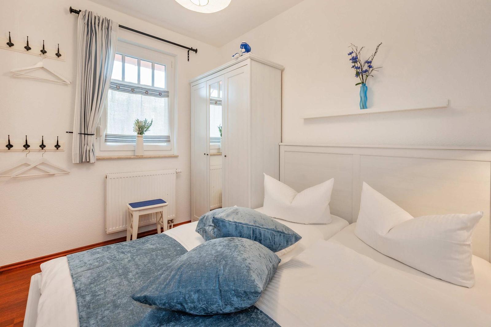 Schlafzimmer mit Doppelbett, Kleiderständer und Fenster mit Vorhängen.