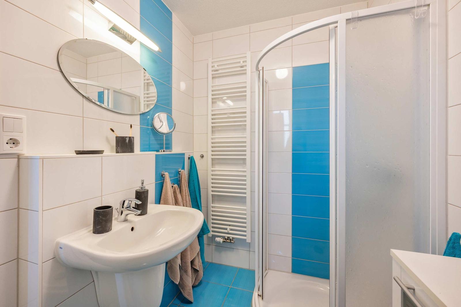 Badezimmer mit Dusche, Waschbecken und Heizkörper an der Wand.