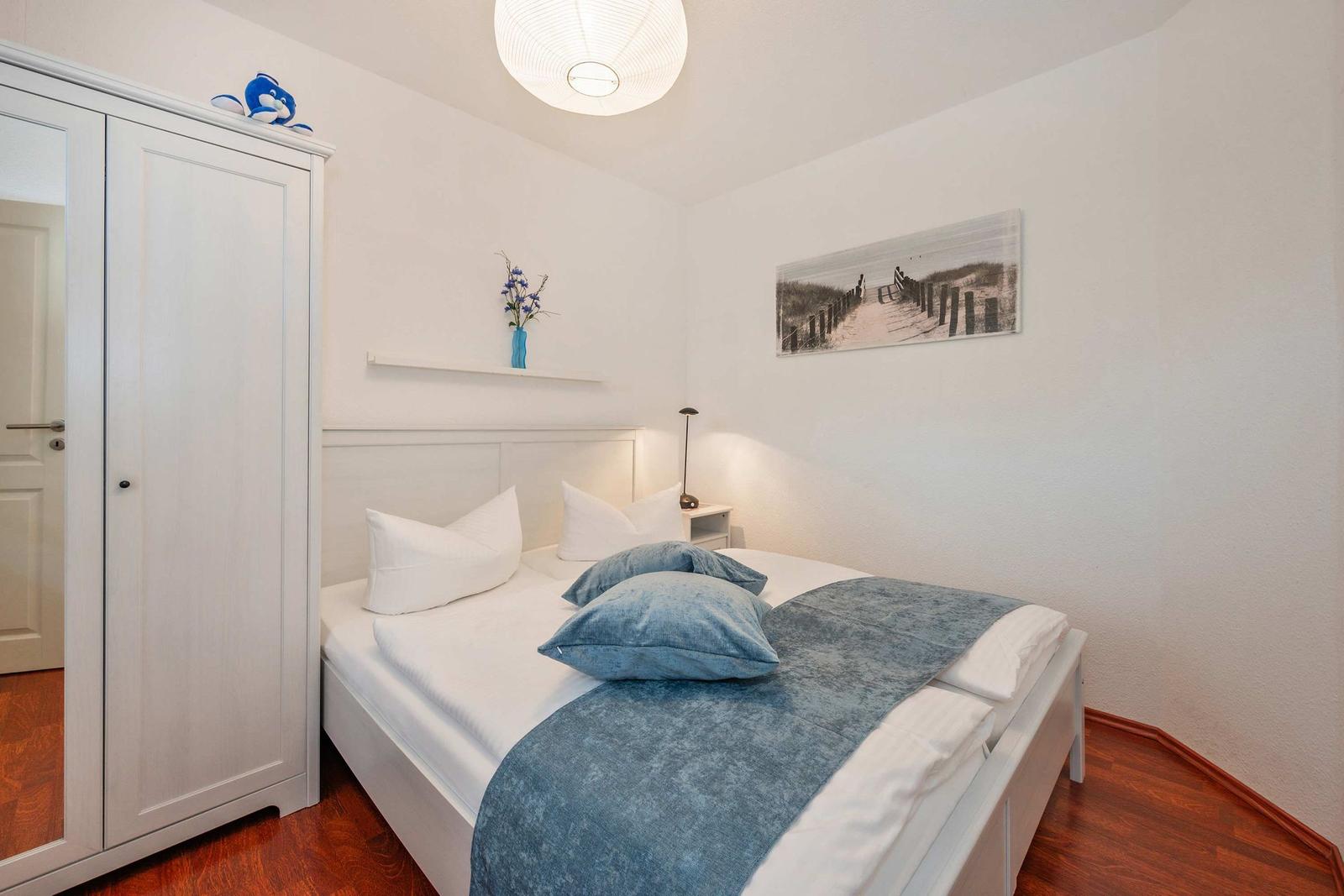 Schlafzimmer mit weißem Bett, blauen Kissen und Holzboden.