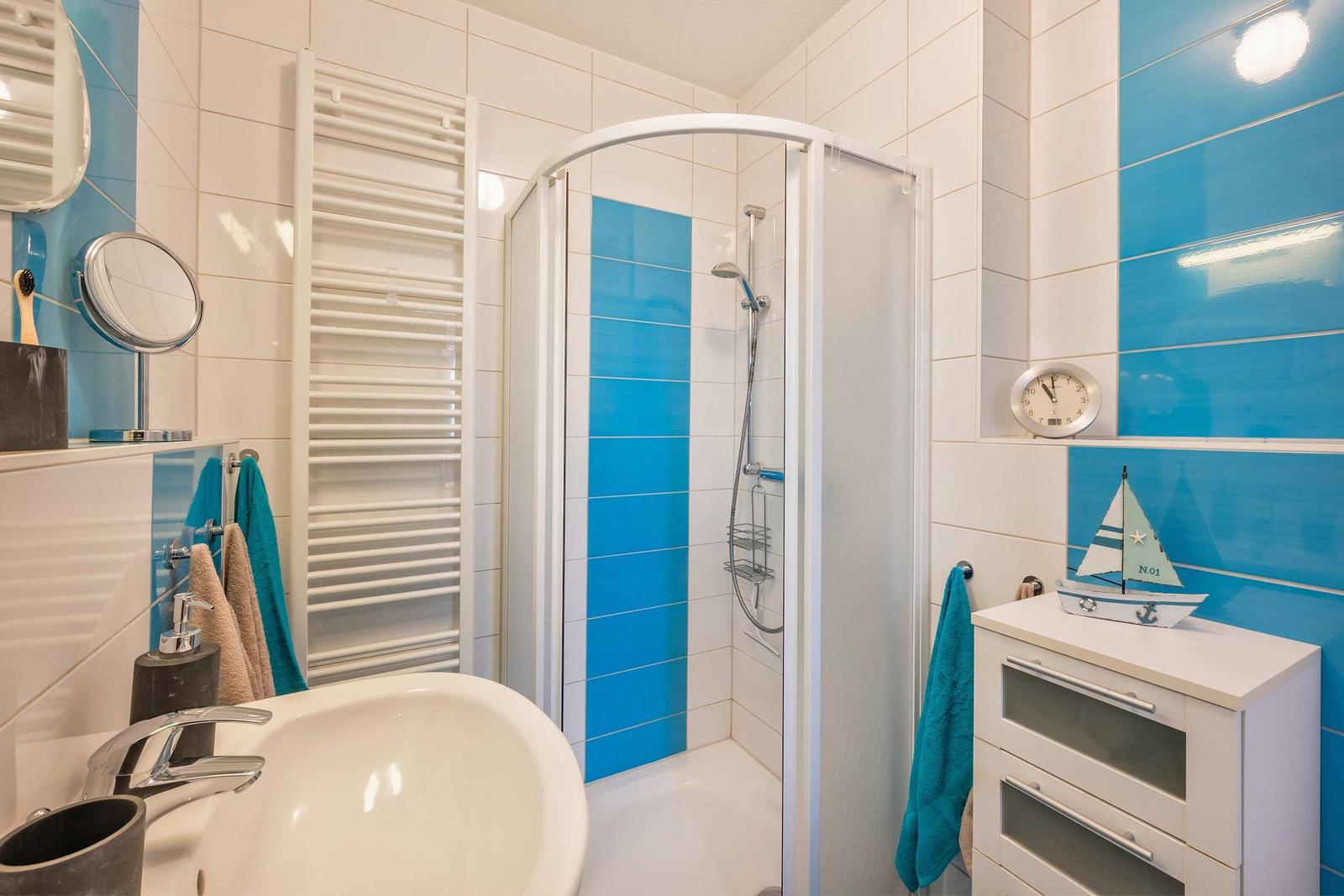 Badezimmer mit Dusche, Waschbecken und Schrank. Blaue und weiße Fliesen.