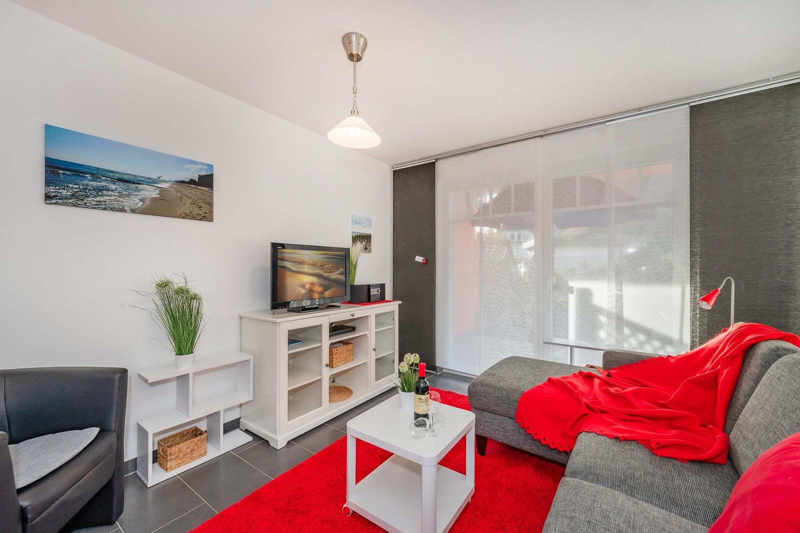 Wohnzimmer mit Sofa, Couchtisch und Fernseher. Roter Teppich und Wandbild.