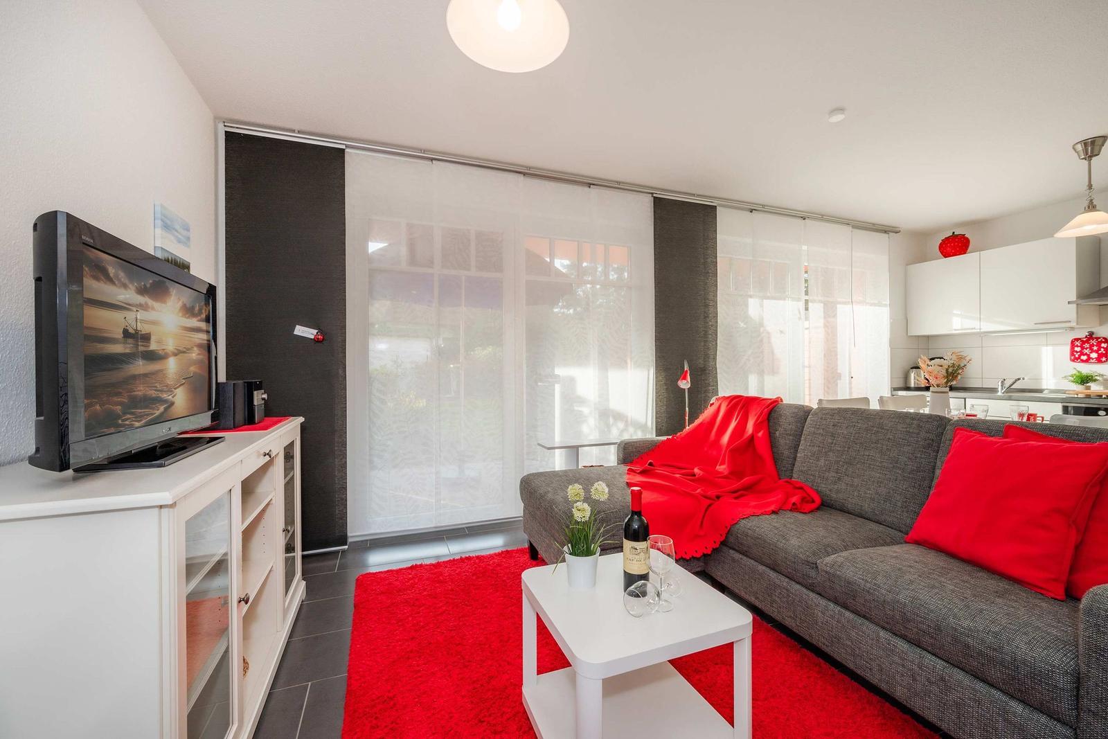 Wohnzimmer mit grauem Sofa, rotem Teppich und Fernseher auf weißen Schrank.