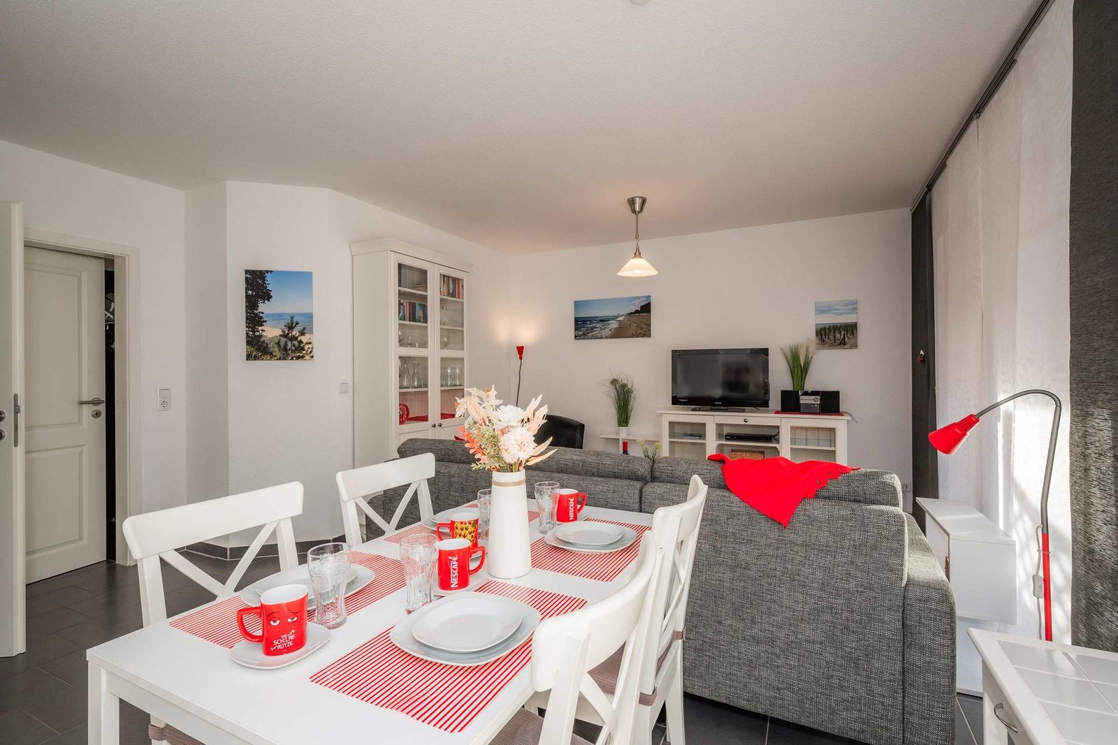 Esszimmer mit Tisch, Stühlen und Sofa. Wandbilder und TV sichtbar.