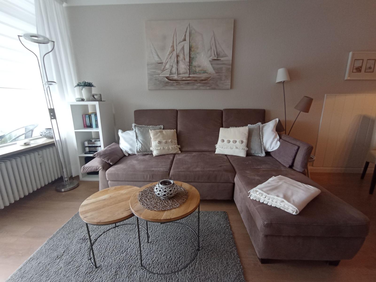 A living room with a brown sofa, two round wooden tables, and wall art.