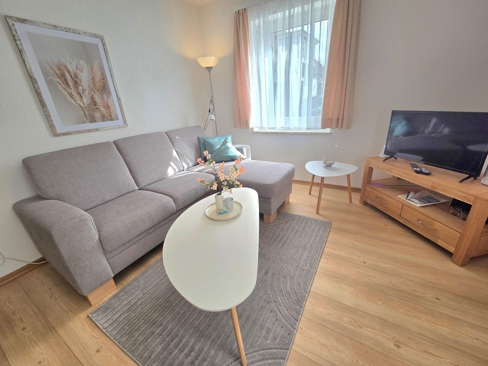 Ein Wohnzimmer mit grauem Sofa, weißem Tisch und Holzboden.