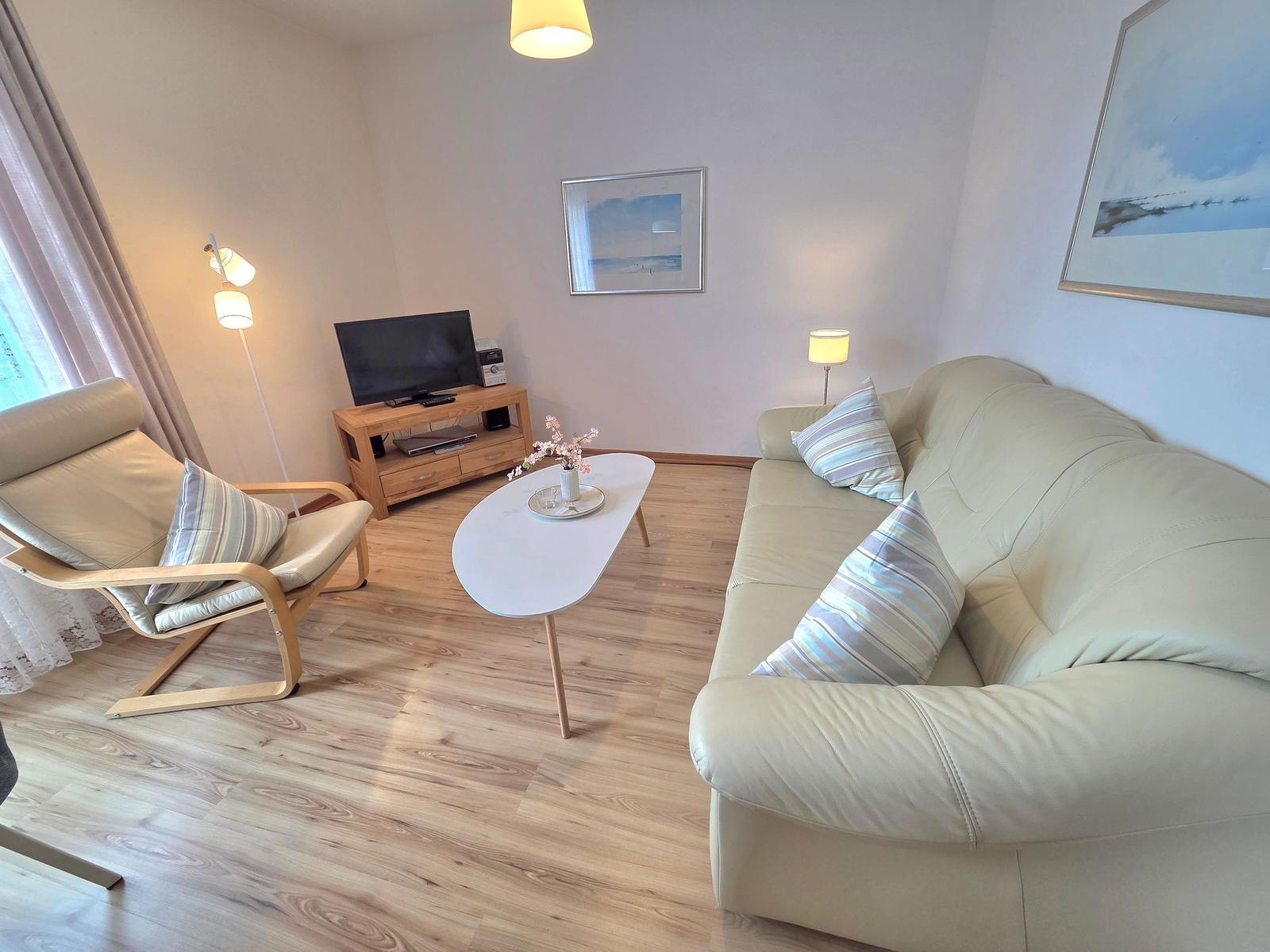 Wohnzimmer mit Sofa, Sessel, Couchtisch und Fernseher auf Holzregal.