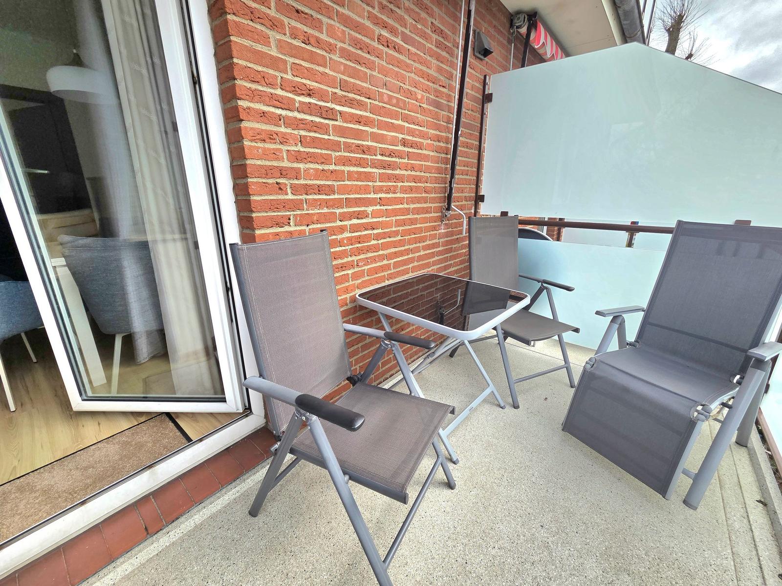 Terrasse mit drei Stühlen und Tisch vor rotem Backsteinhaus