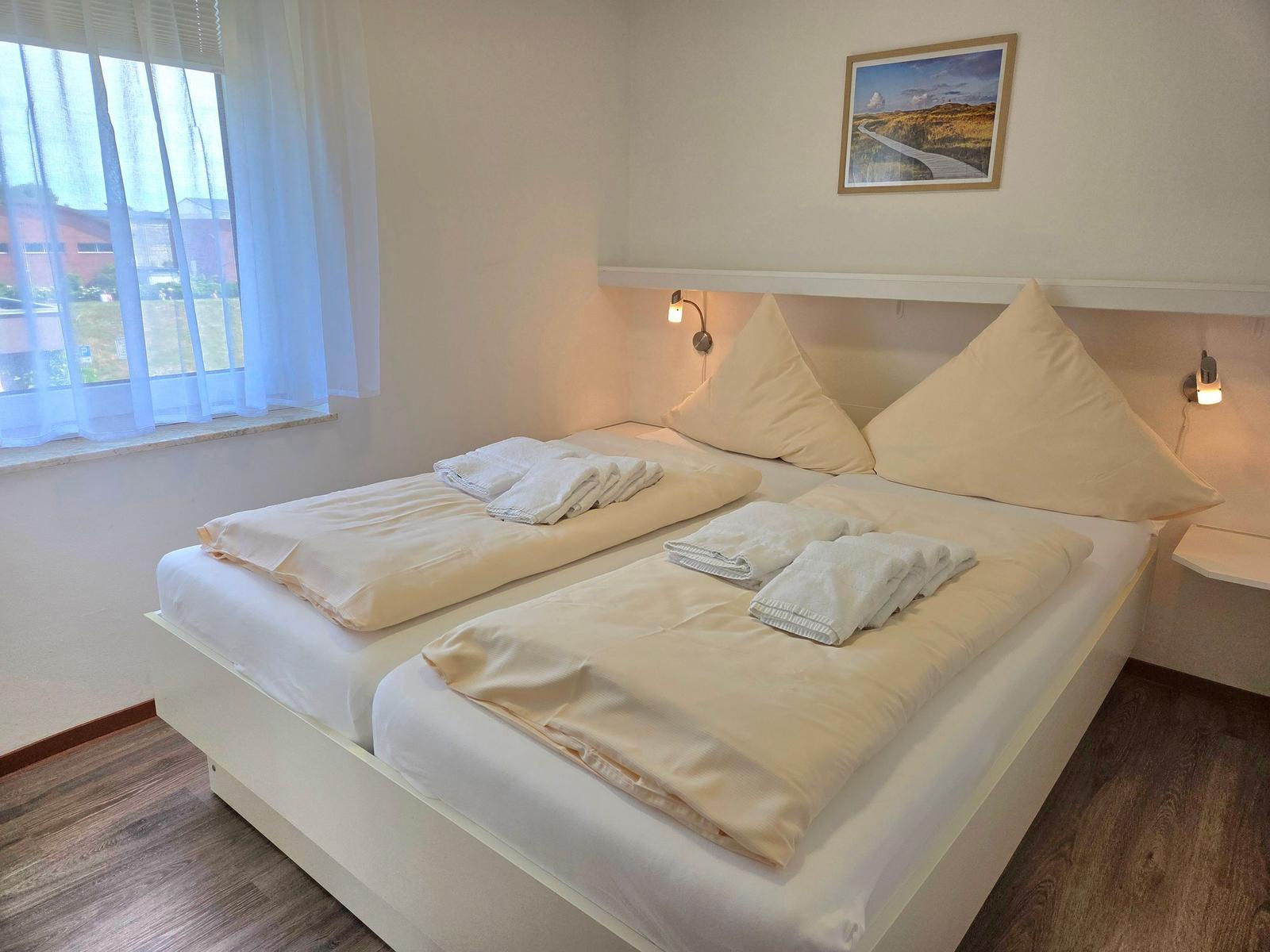 Zimmer mit Doppelbett, Fenster und Wandbild. Beleuchtung an Kopfseite.