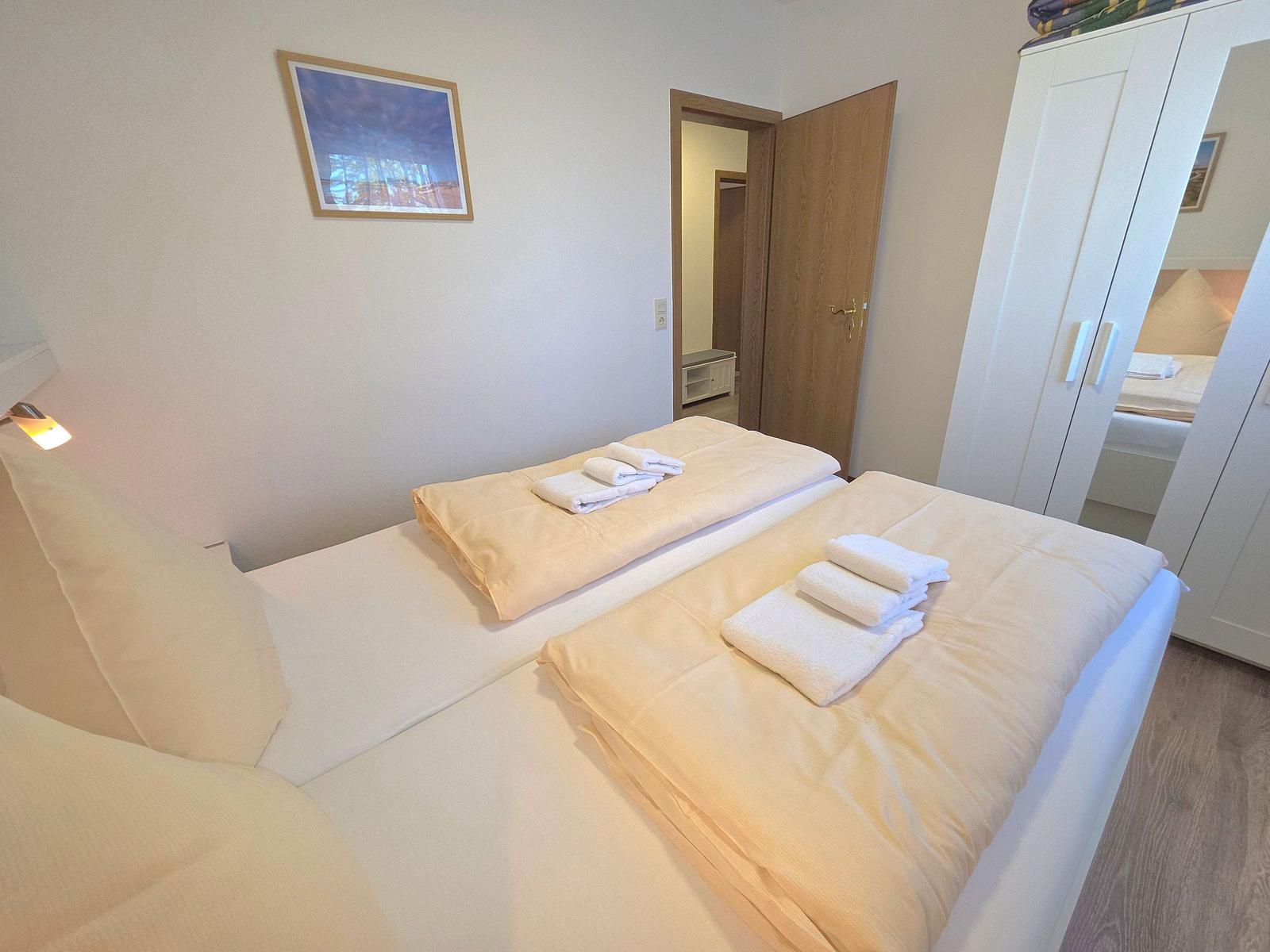 Schlafzimmer mit Bett, Kleiderschrank und Tür zum Bad.