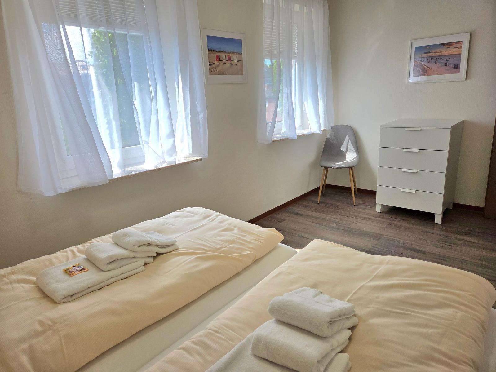 Zwei Betten mit Handtüchern, Fenster mit Vorhängen, Schrank und Stuhl.