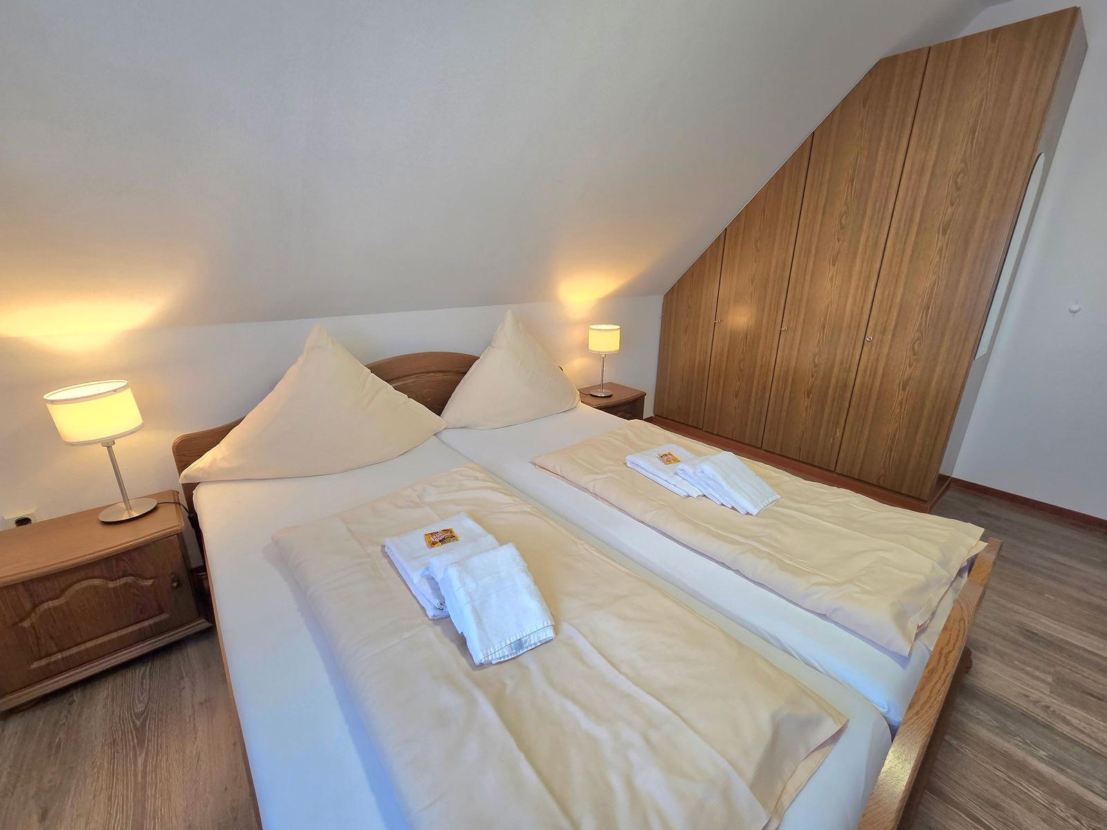 Schlafzimmer mit Doppelbett, Holzmöbel und Stehgarderobe unter Dachschräge.