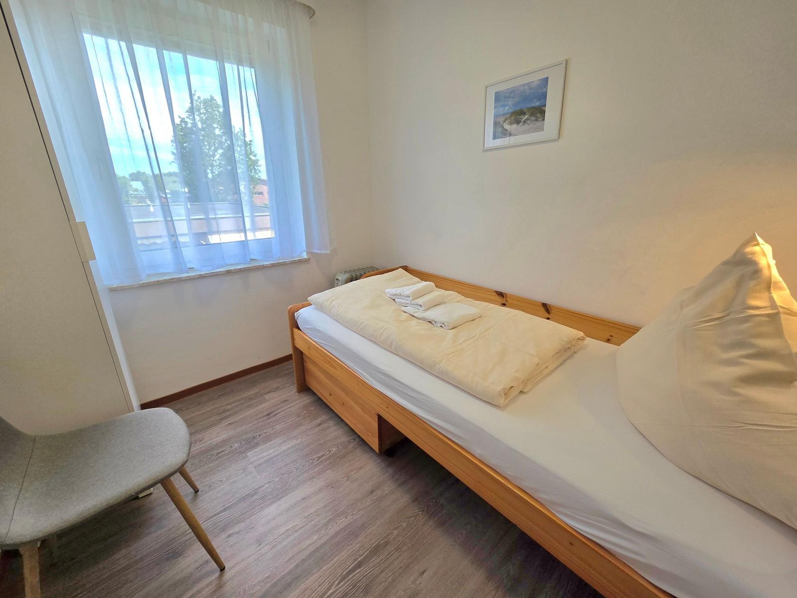 Ein Schlafzimmer mit einem Holzbett, einem Fenster mit Vorhängen und einem Stuhl.