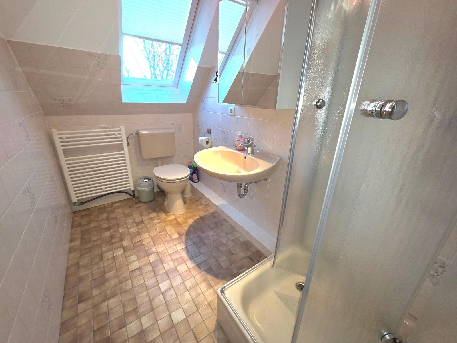 Badezimmer mit Dusche, Waschbecken und Toilette unter Dachschrägen.