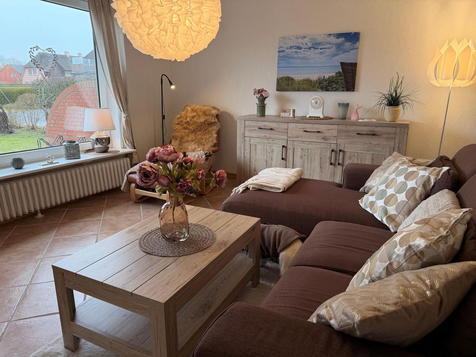 Ein Wohnzimmer mit braunem Sofa, Holztisch und Fensterblick auf die Landschaft.