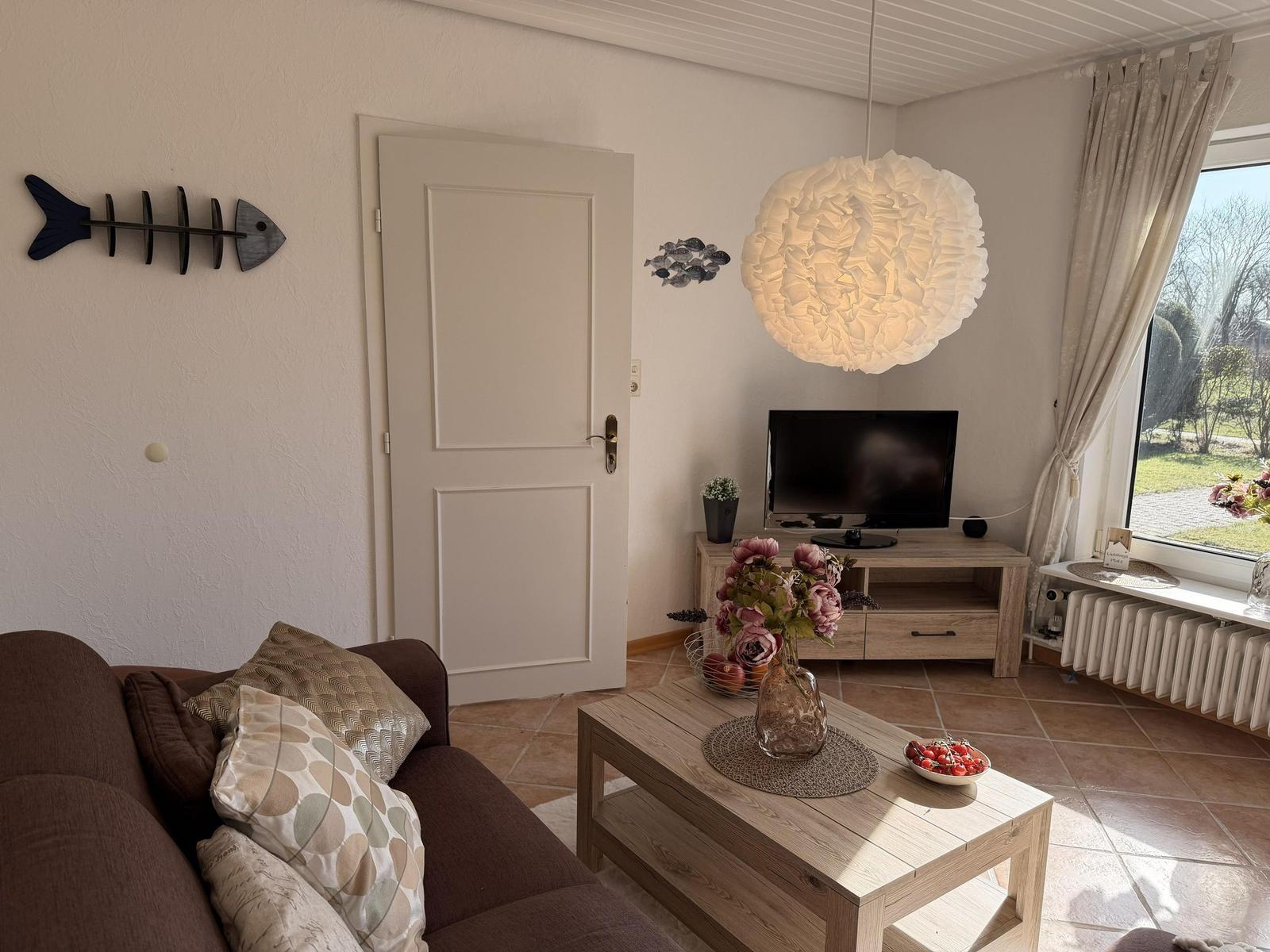 Wohnzimmer mit Sofa, TV, Tisch und Fenster. Wanddekoration und Hängelampe.