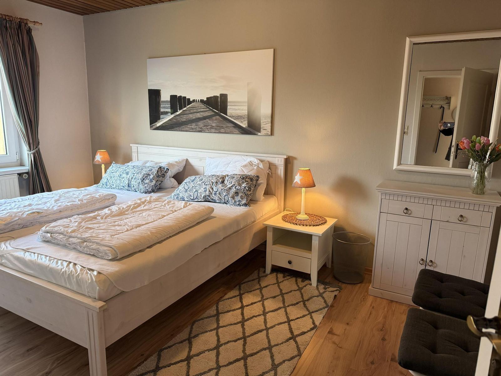 Schlafzimmer mit Doppelbett, Nachttisch, Spiegelschrank und Wandbild.