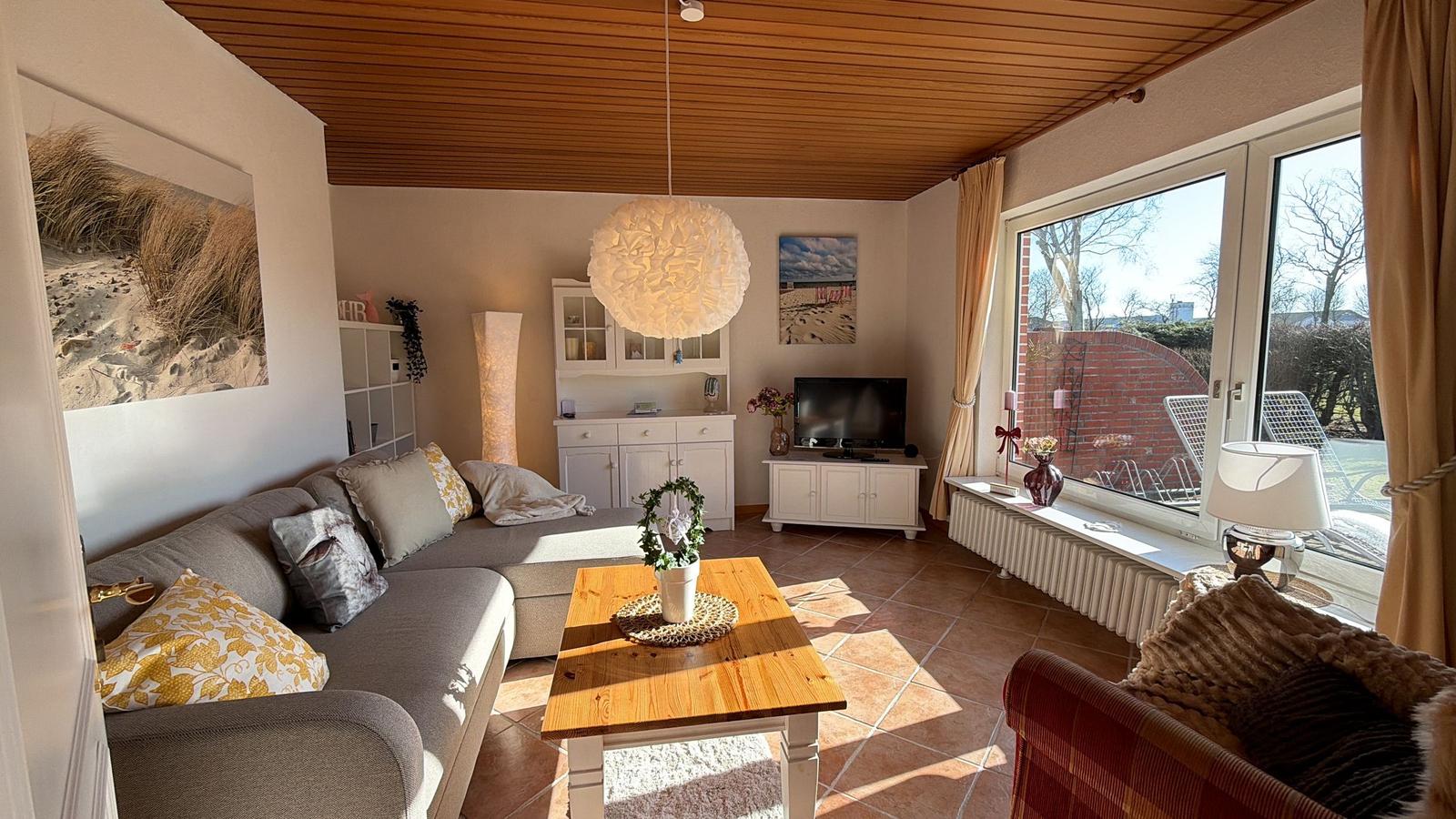 Wohnzimmer mit Sofa, Couchtisch und TV. Große Fenster mit Blick auf Garten.