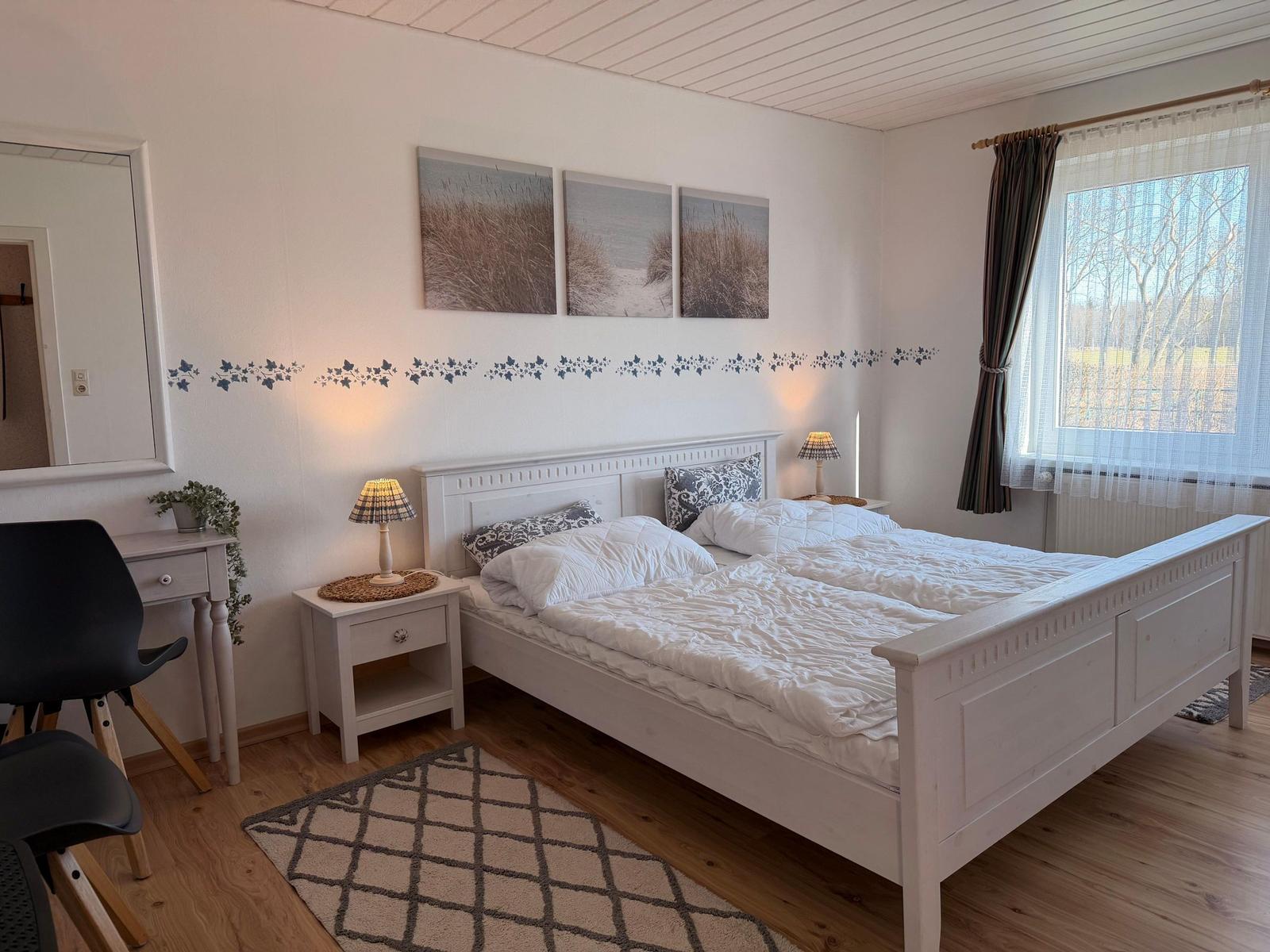 Schlafzimmer mit Doppelbett, Nachttischen und Fenster mit Vorhängen.