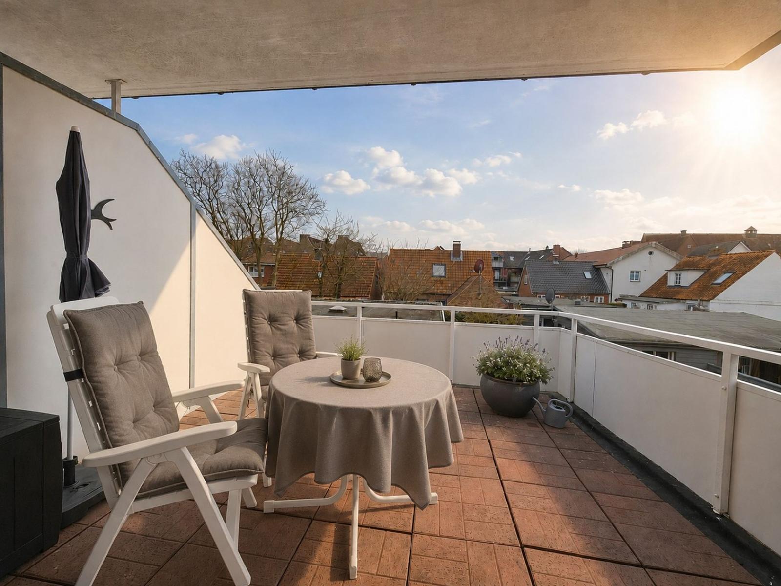 Terrasse mit Tisch, zwei Stühlen, Pflanzen und Blick auf Dächer.