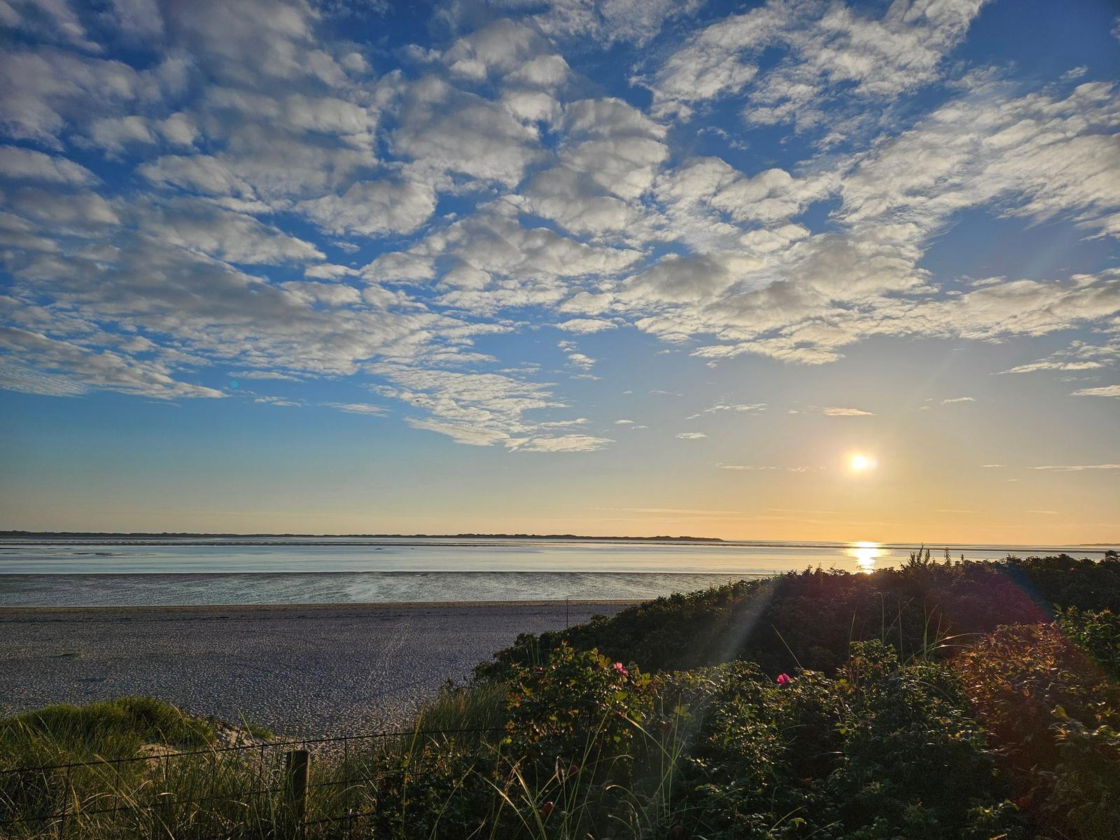 Sonnenuntergang über Watt und Strand mit bewölktem Himmel