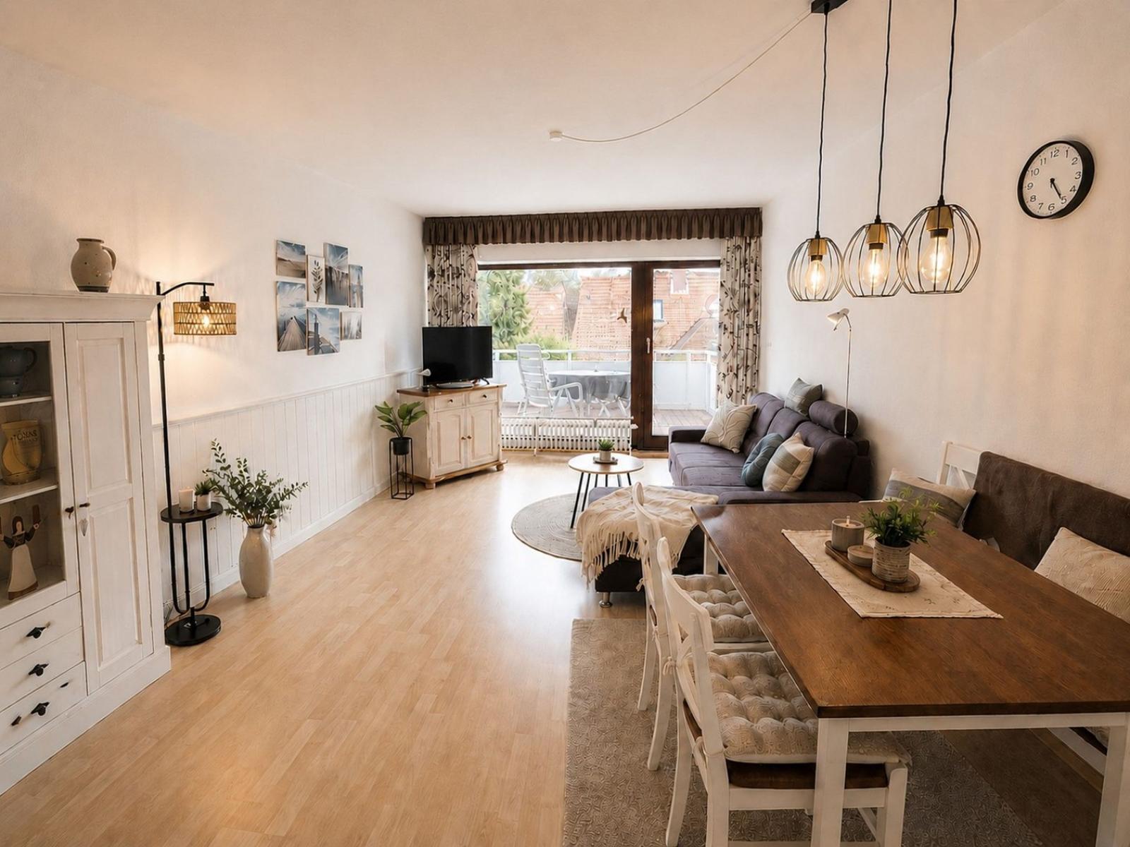 Wohn- und Essbereich mit Holzboden, Sofa, Esstisch und Balkonzugang.