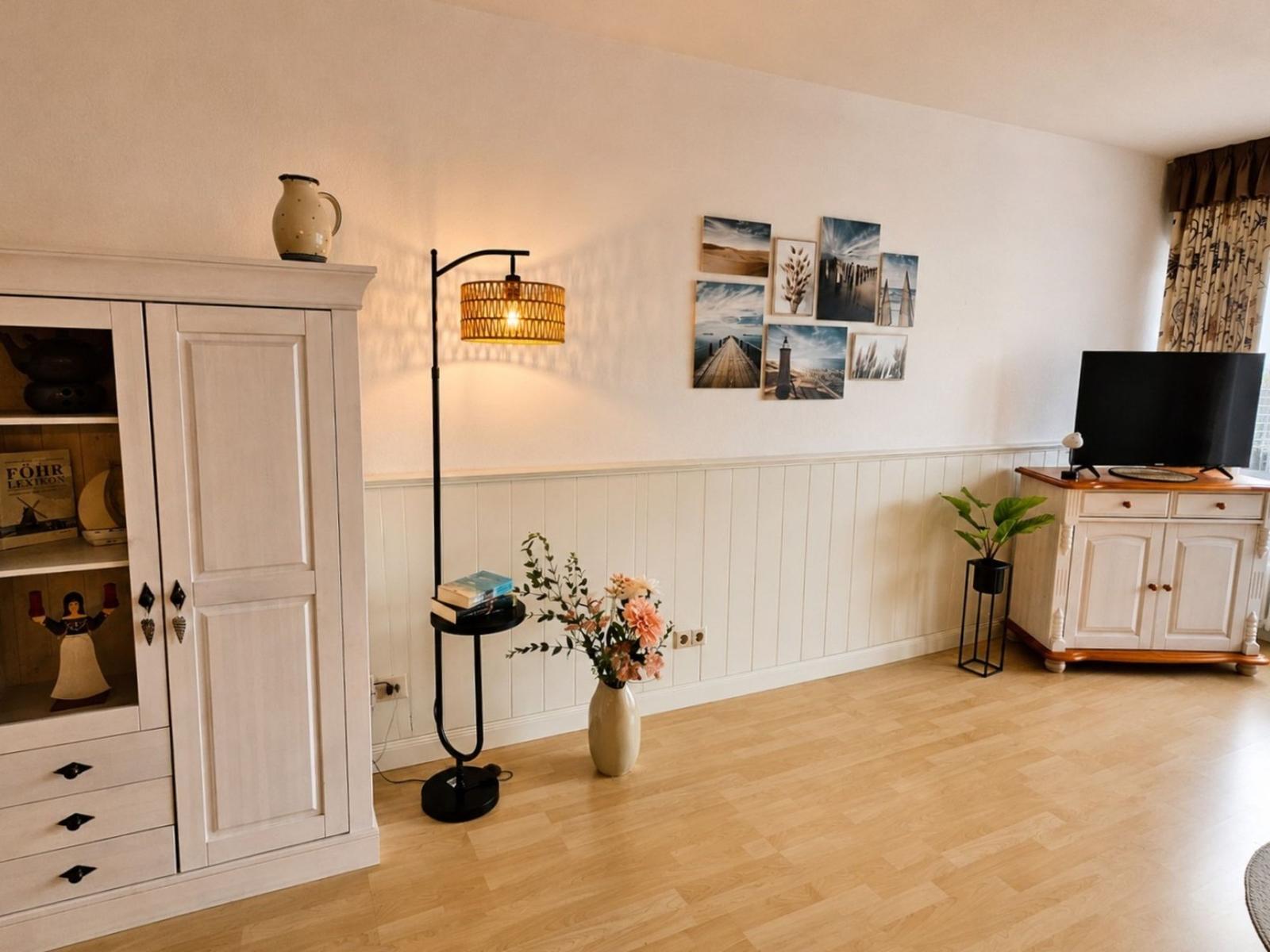 Wohnzimmer mit Holzboden, weißen Schränken und Wandbildern an der Wand.