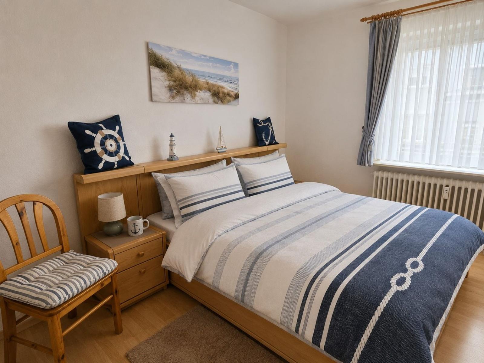 Schlafzimmer mit Bett, Nachttisch, Stuhl und Wandbild mit Strandmotiv.