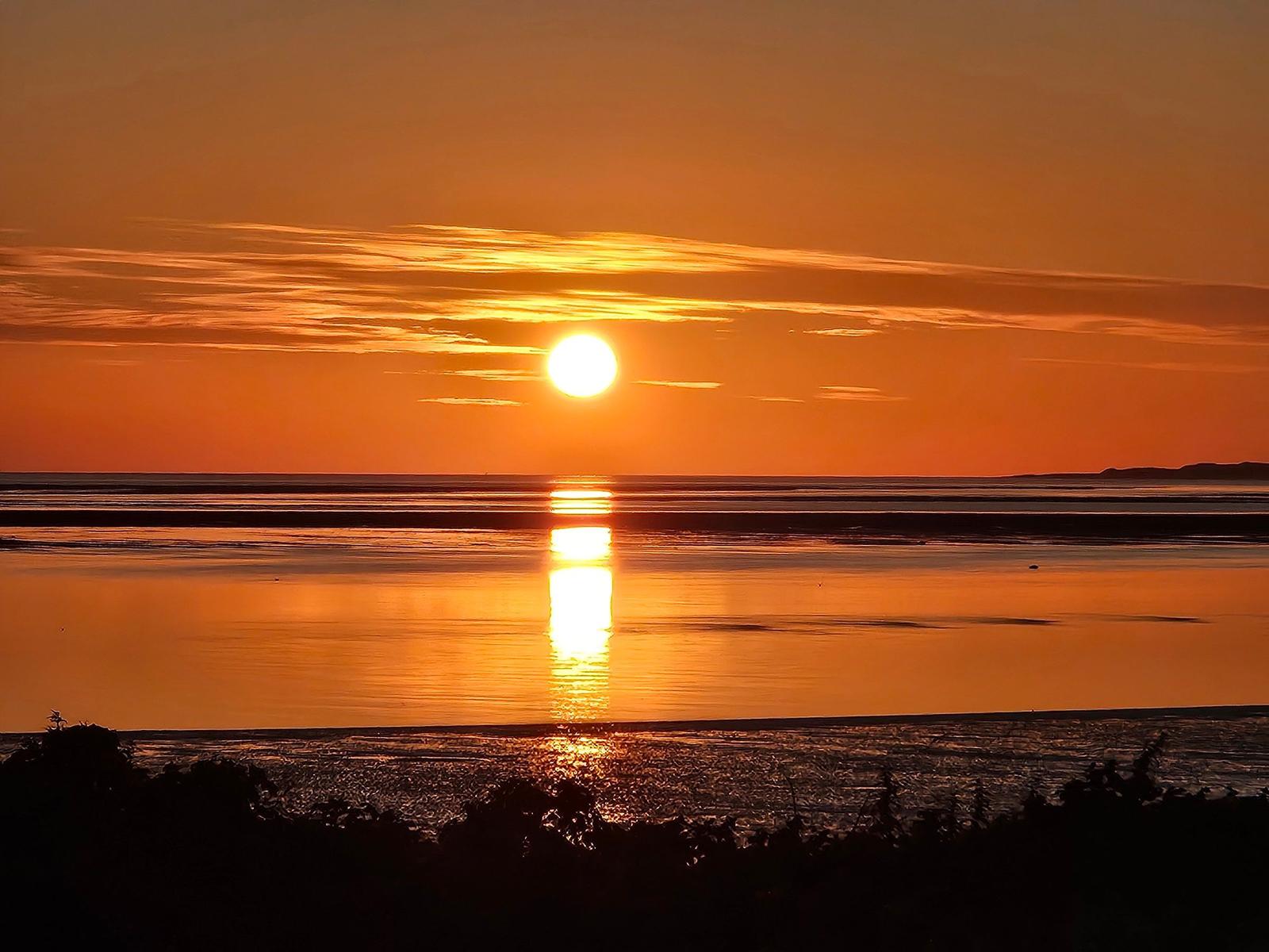 Sonnenuntergang über ruhigem Meer mit orangefarbenem Himmel und Reflexion.