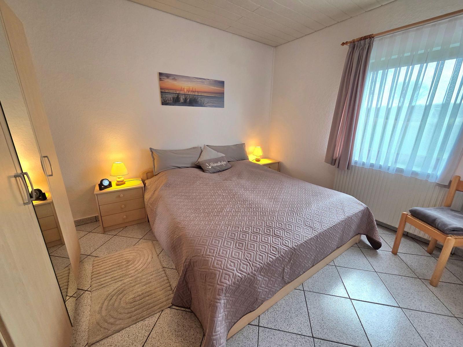 Schlafzimmer mit Doppelbett, Nachttischen und Fenster mit Vorhängen.