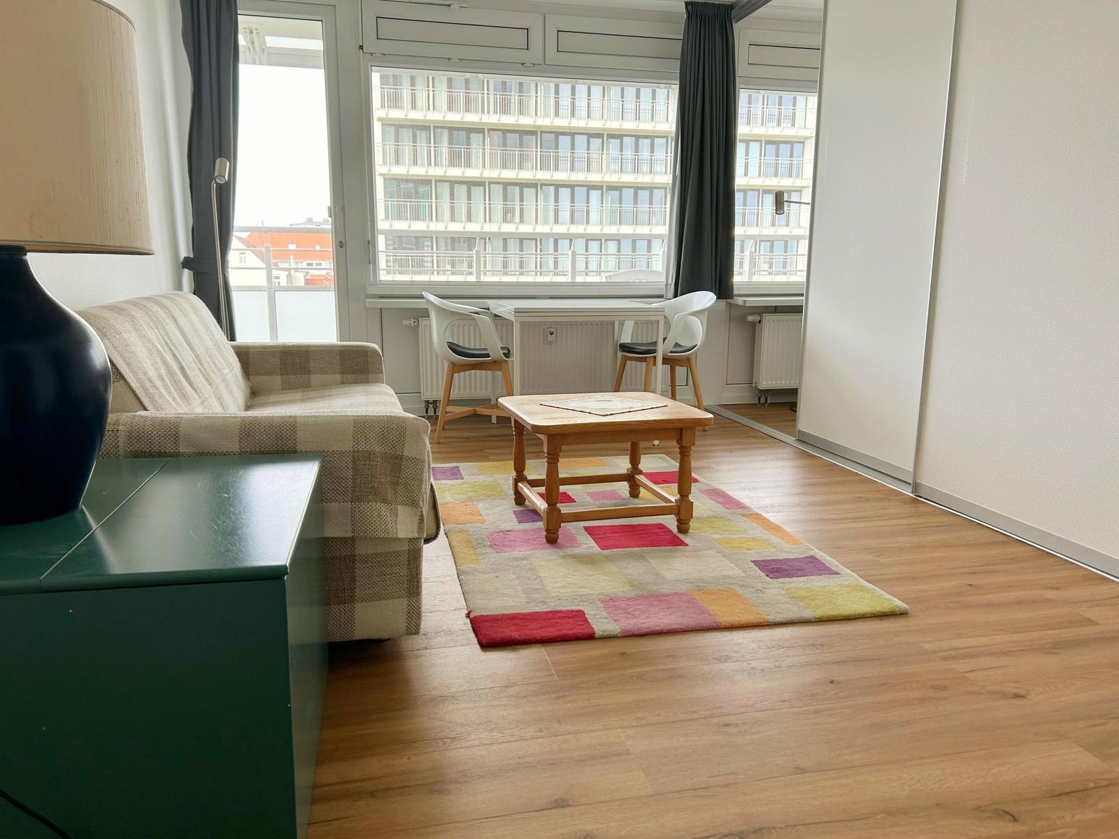 Wohnzimmer mit Sofa, Tisch und Fensterblick auf Gebäude.