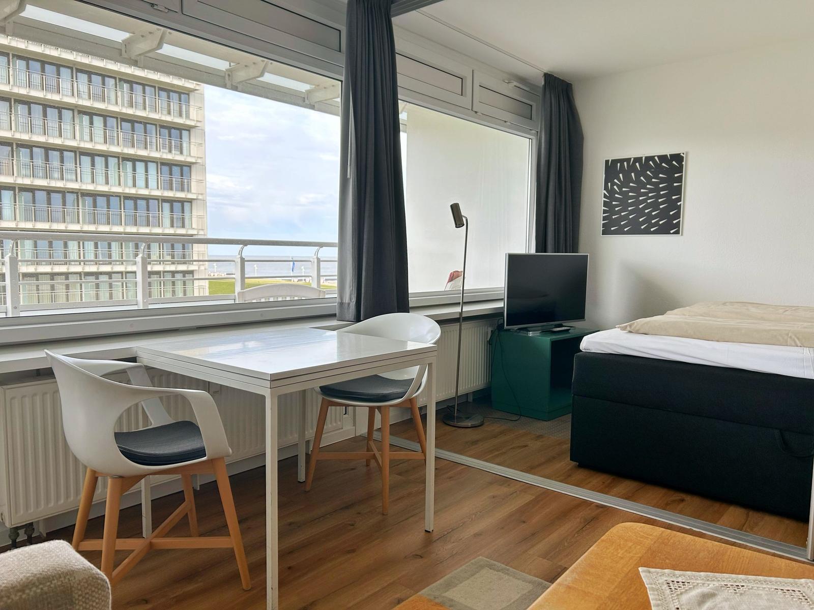 Zimmer mit Bett, Schreibtisch und Balkonblick auf Gebäude und Meer.