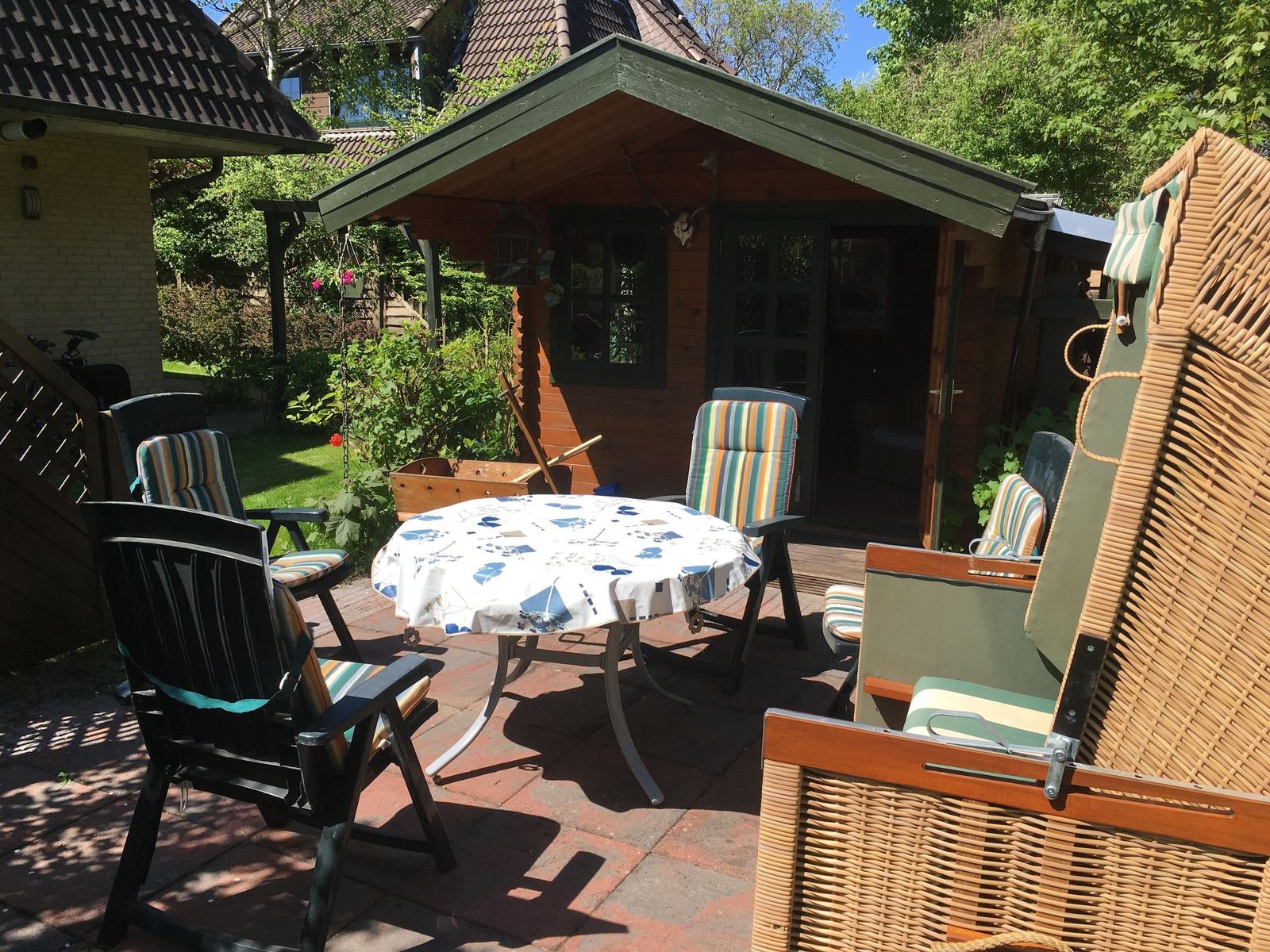 Terrasse mit Tisch, Stühlen und Hütte im Hintergrund.