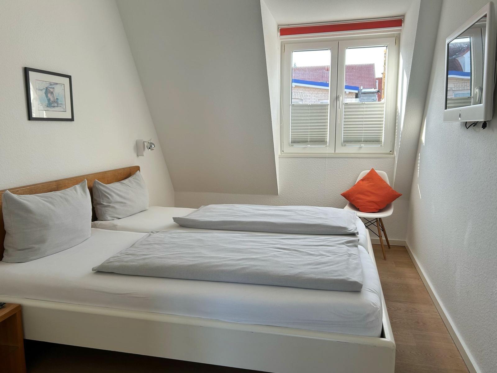Ein Schlafzimmer mit Doppelbett, Fenster und Wandspiegel.