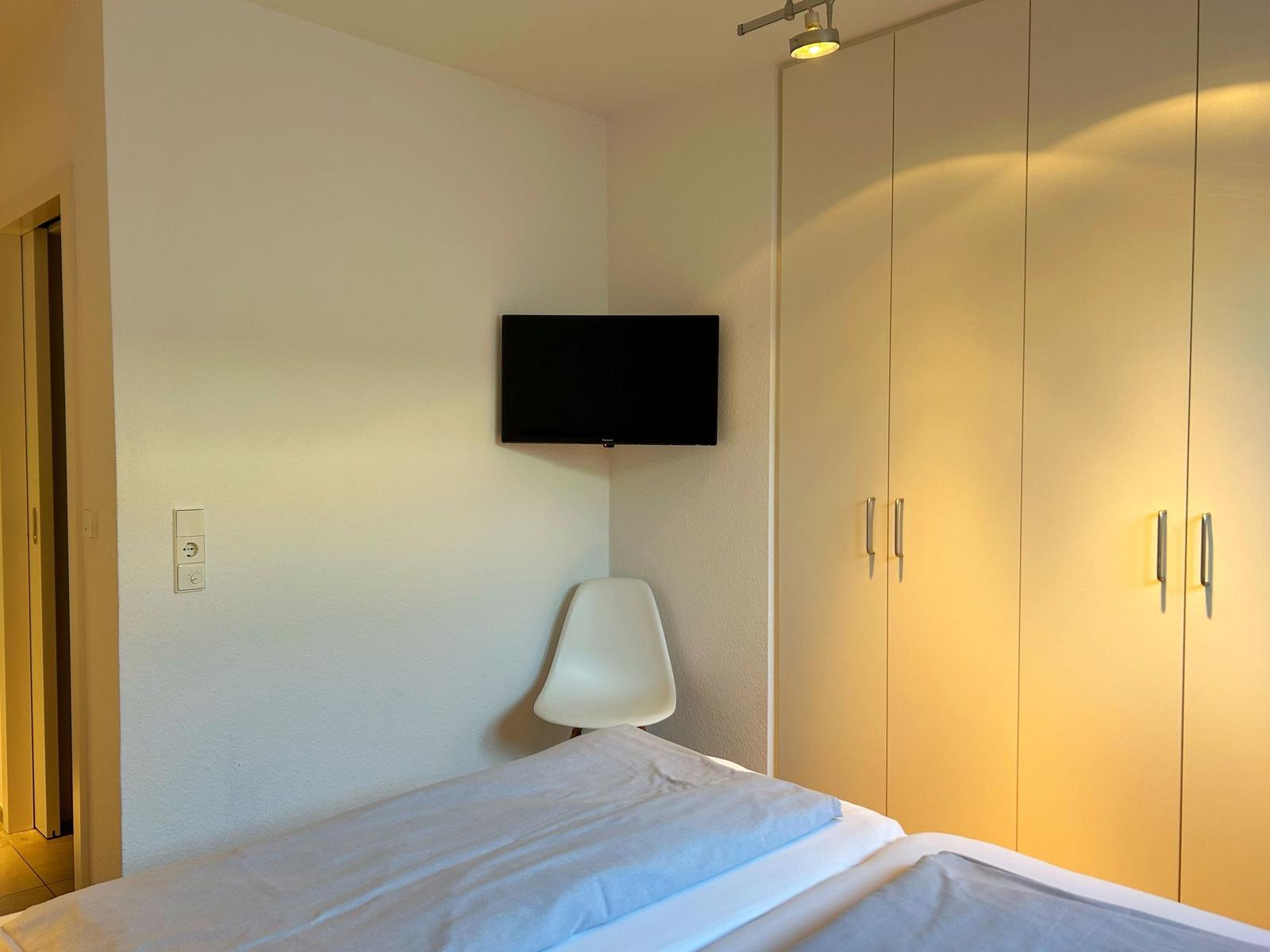 Schlafzimmer mit Bett, Kleiderschrank und Wand-TV.