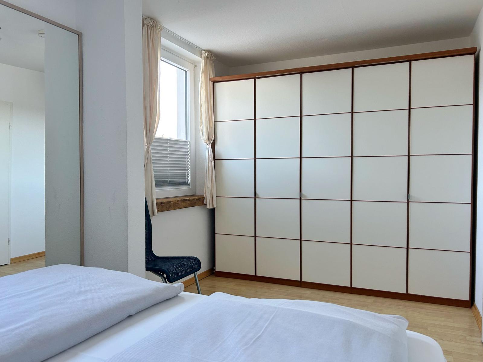 Schlafzimmer mit Bett, Kleiderschrank und Fenster mit Vorhängen.