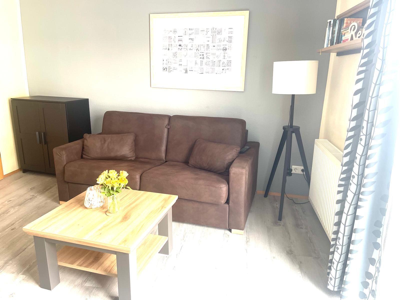 Ein Wohnzimmer mit braunem Sofa, Holztisch und Stehlampe.