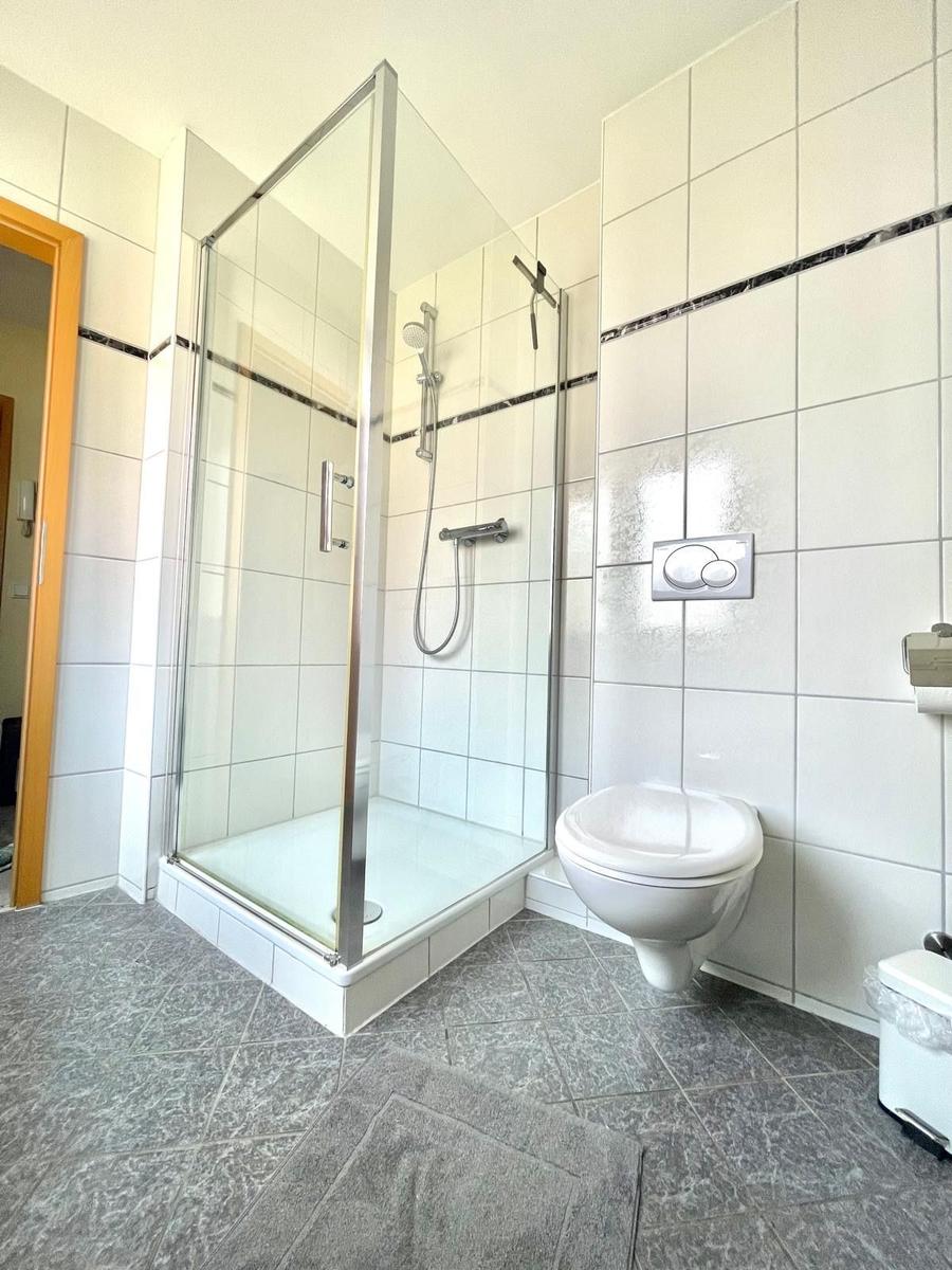 Badezimmer mit Dusche, WC und Fliesenboden.